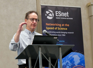 Photo of person standing at podium speaking, with ESnet sign behind them.